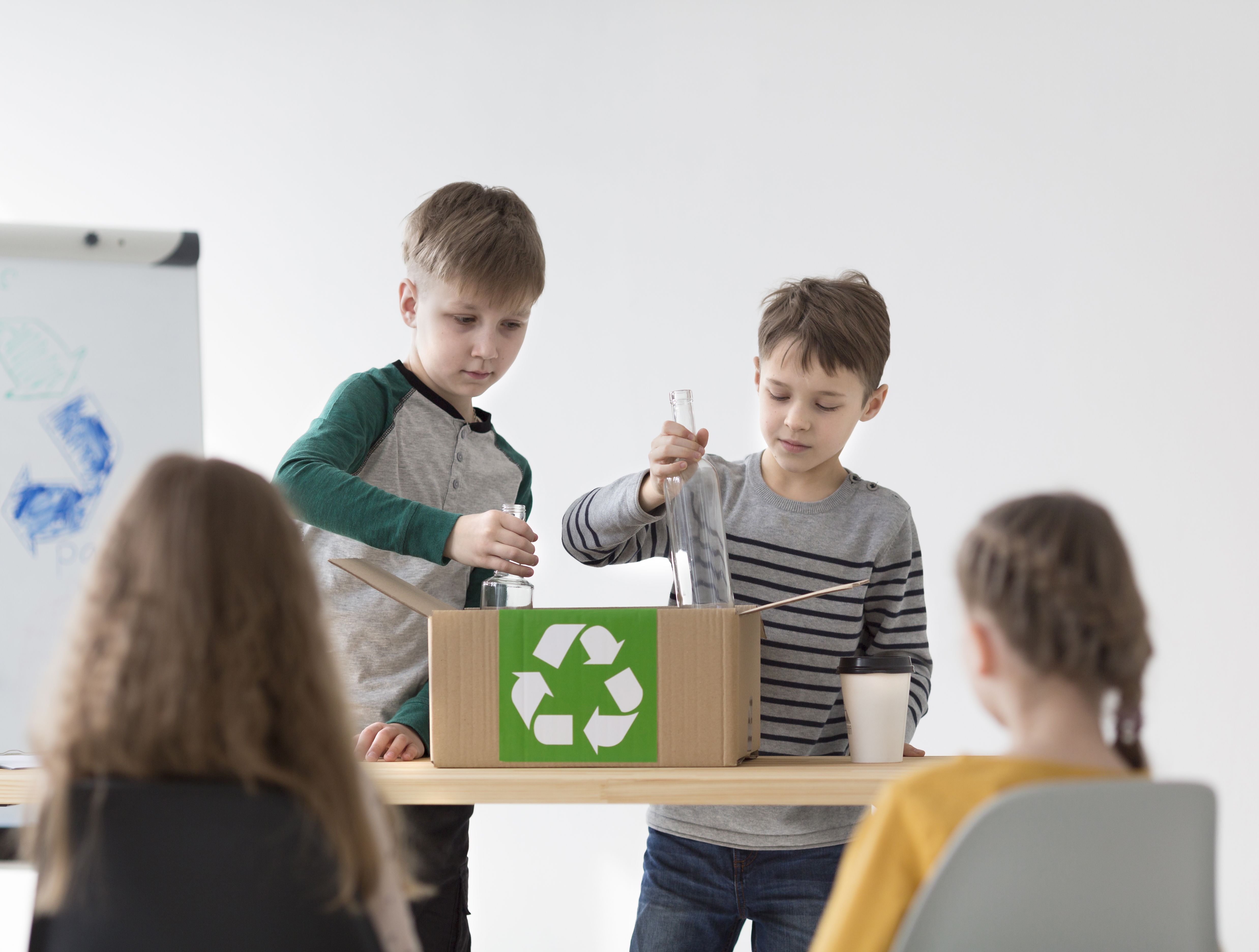 Deux écoliers apprennent à trier et recycler une bouteille en verre dans le bon bac de tri.
